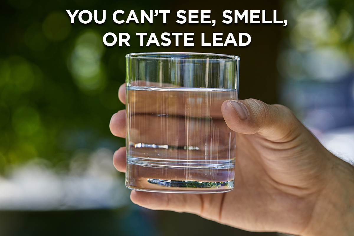 A hand holding a glass of clear water with text, you cannot see, smell or taste Lead